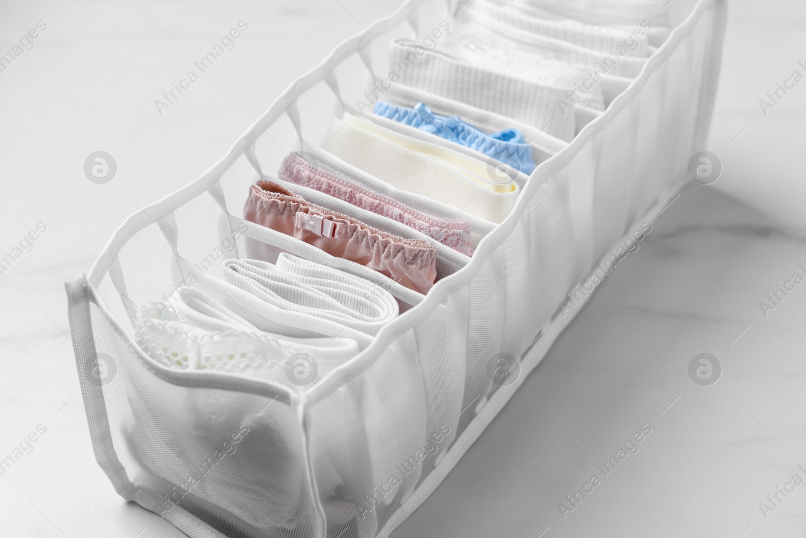 Photo of Organizer with folded women's underwear on white marble table, closeup