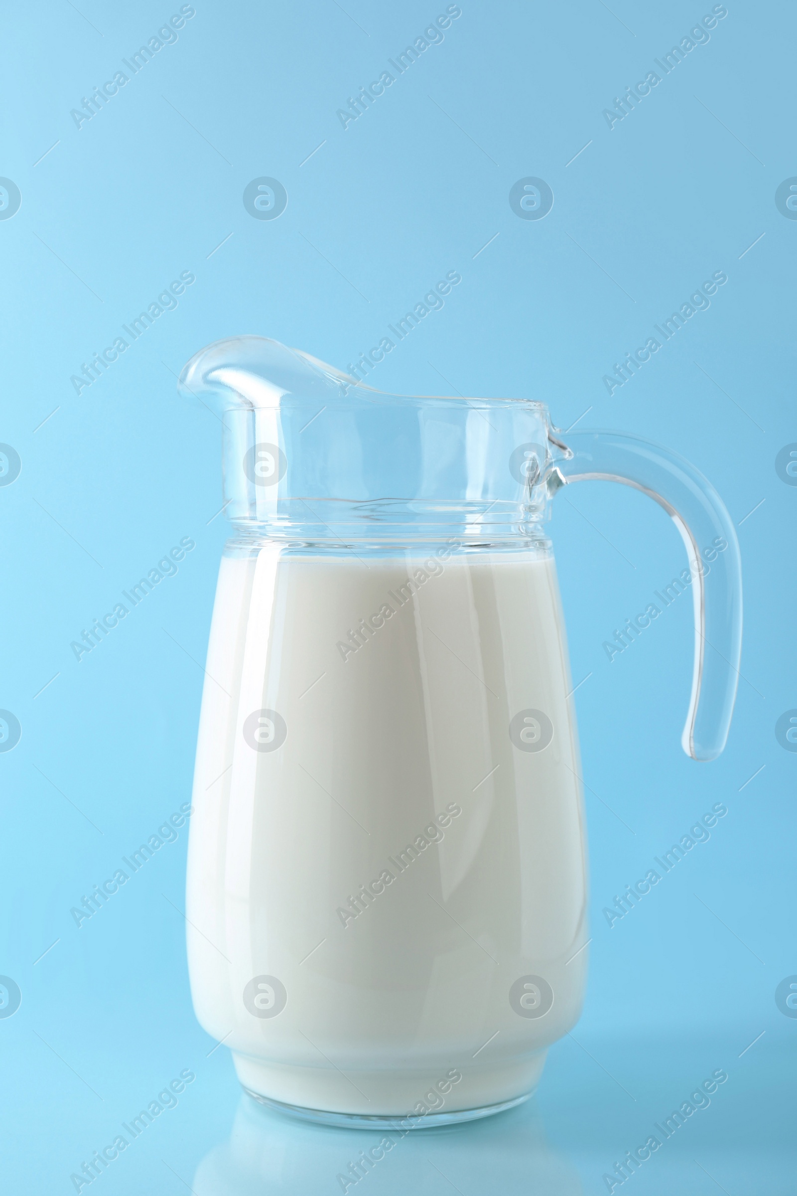 Photo of Jug of fresh milk on light blue background