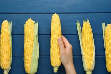 Photo of Woman with corncob on blue wooden table, top view