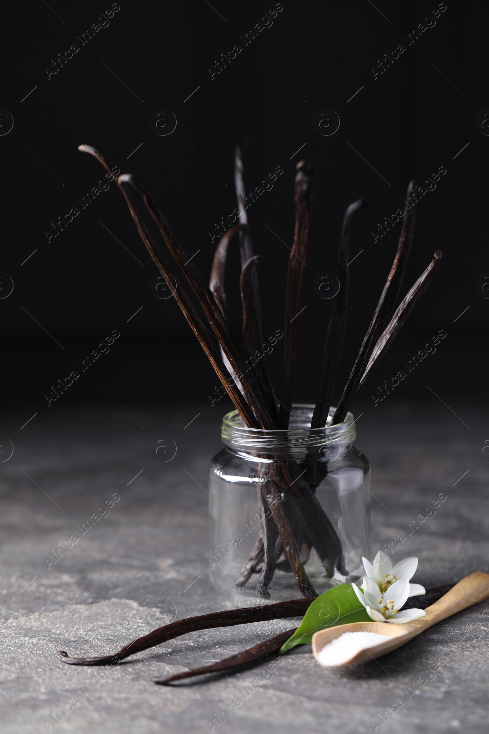 Photo of Spoon with sugar, flowers, leaf and vanilla pods on grey textured table