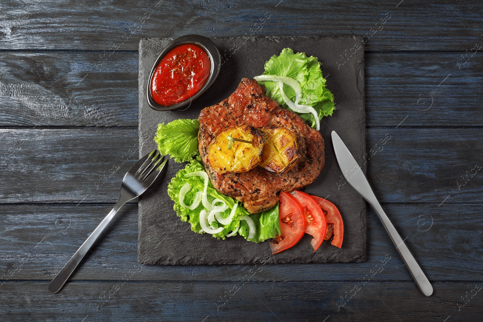 Photo of Slate plate with tasty grilled meat, potatoes and sauce on table, top view