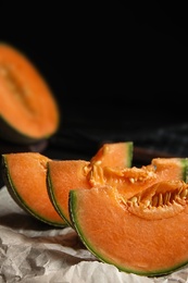Photo of Slices of ripe cantaloupe melon on parchment against black background. Space for text