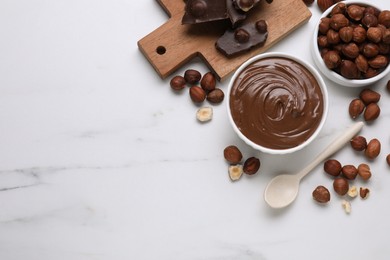 Photo of Bowl with tasty paste, chocolate pieces and nuts on white marble table, flat lay. Space for text