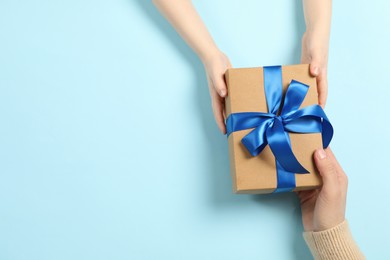 Photo of Mother giving gift box to her child on light blue background, top view. Space for text