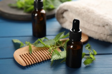 Photo of Stinging nettle extract, green leaves and comb on blue wooden table, closeup. Natural hair care