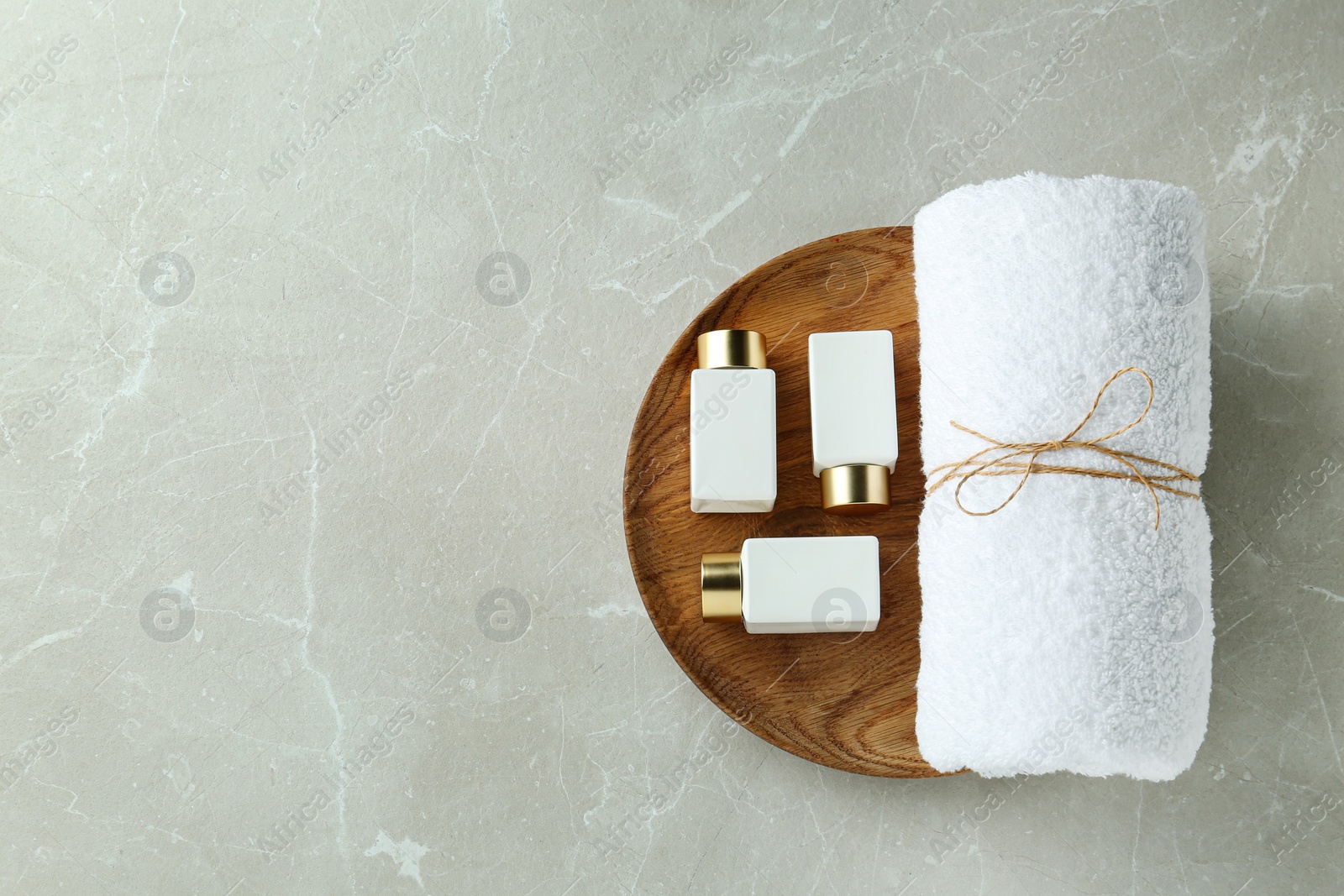 Photo of Top view of wooden tray with cosmetic bottles and towel on light grey marble table, space for text. Spa treatment