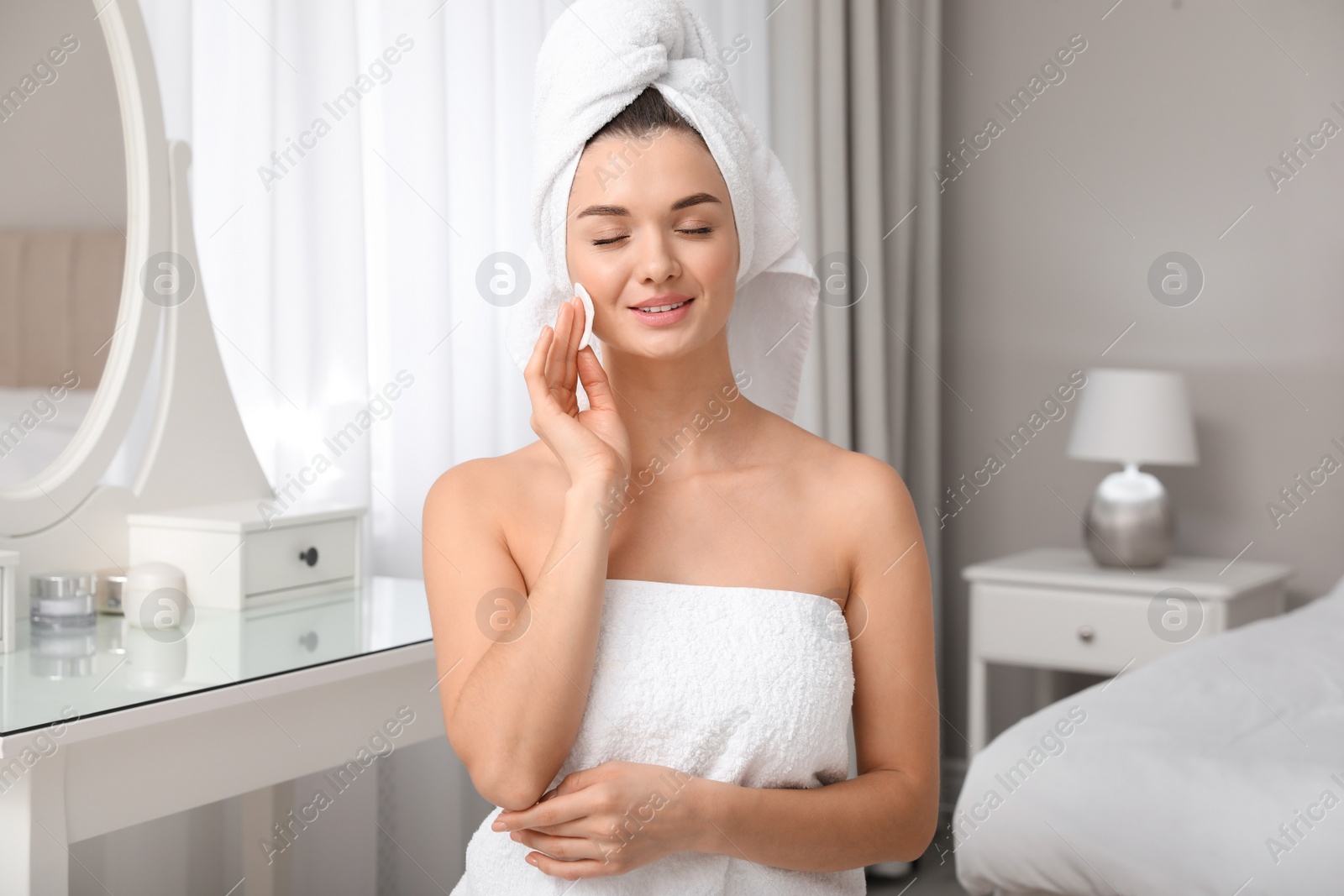 Photo of Beautiful young woman with hair wrapped in towel cleaning her face at home