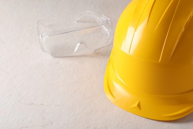 Photo of Hard hat and goggles on white table, closeup with space for text. Safety equipment