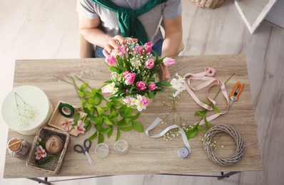 Male decorator creating beautiful bouquet at table, top view