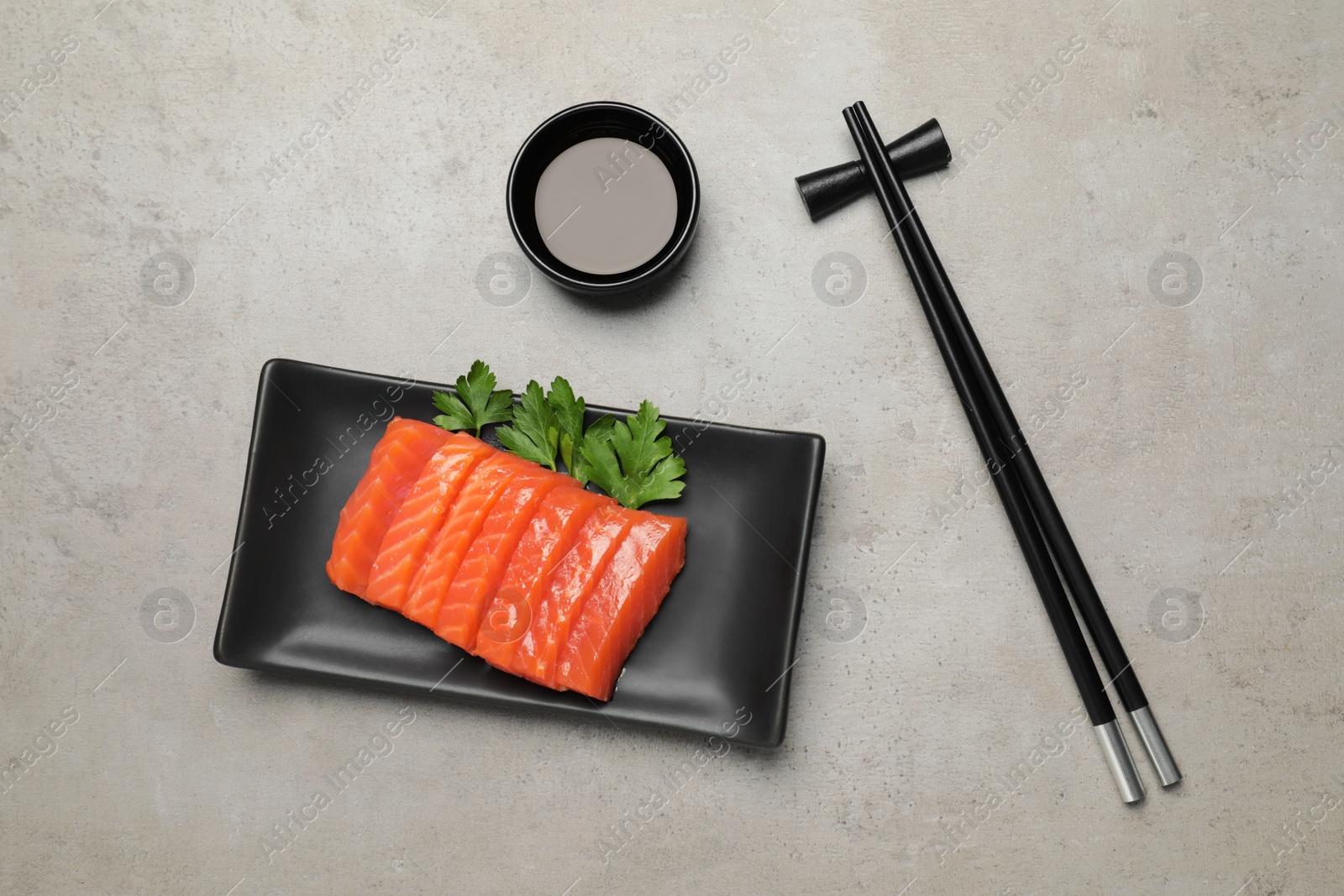 Photo of Plate of tasty salmon slices, soy sauce and parsley on grey table, flat lay. Delicious sashimi dish