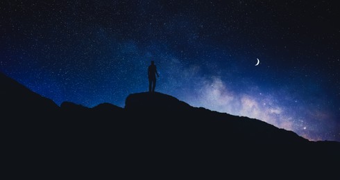 Image of Silhouette of man in mountains under beautiful starry sky with crescent moon at night, banner design