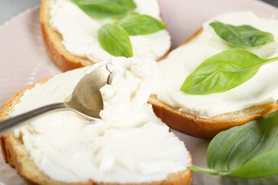 Photo of Delicious sandwiches with cream cheese and basil leaves on plate, closeup