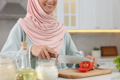 Photo of Muslim woman making delicious salad with vegetables at white table in kitchen, closeup