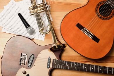 Photo of Guitars, trumpet, microphone and note sheets on wooden background, flat lay. Musical instruments