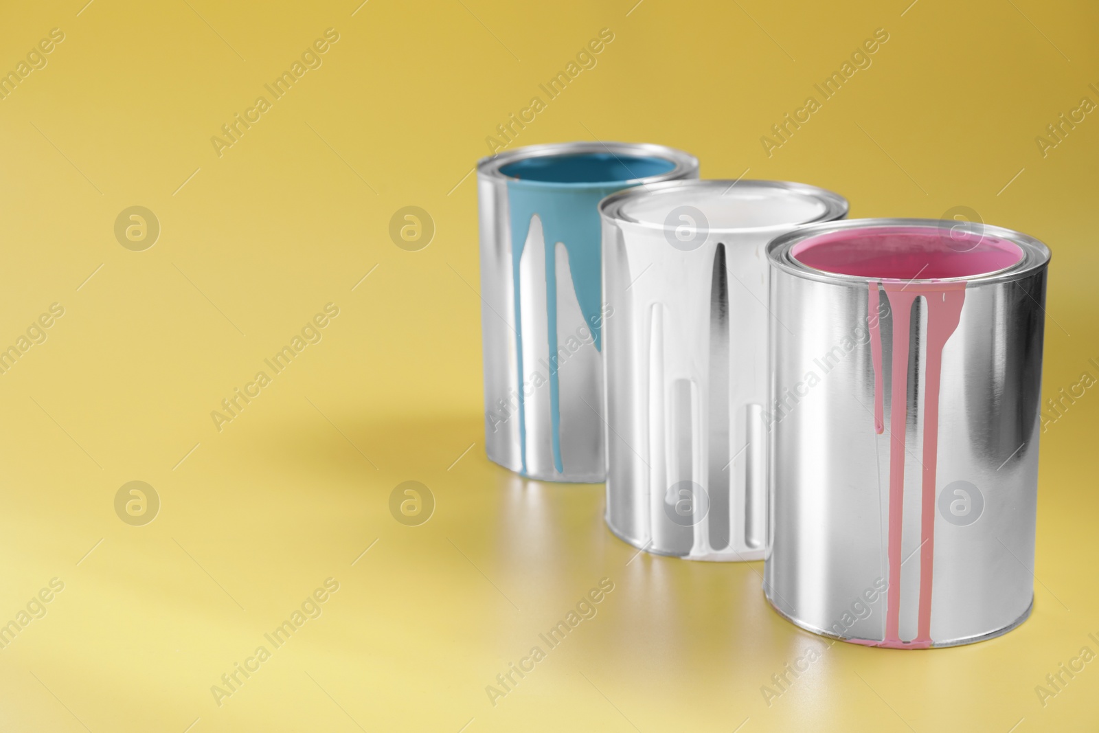 Photo of Cans of paints on yellow background, space for text