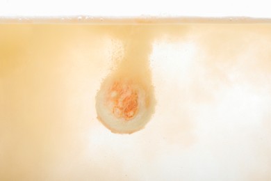 Beige bath bomb dissolving in clear water
