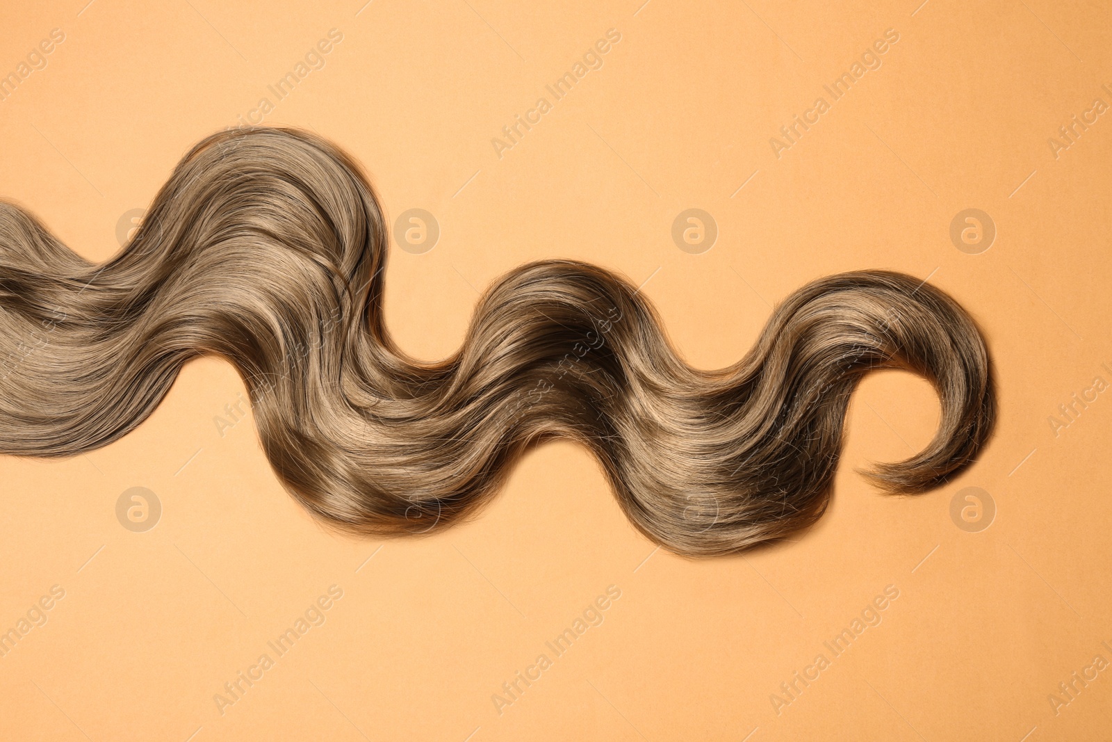 Photo of Lock of brown wavy hair on color background, top view