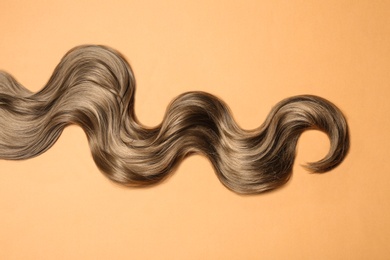 Photo of Lock of brown wavy hair on color background, top view