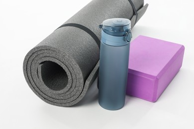 Photo of Grey exercise mat, yoga block and bottle of water isolated on white