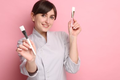 Photo of Cosmetologist with cosmetic brushes on pink background, selective focus