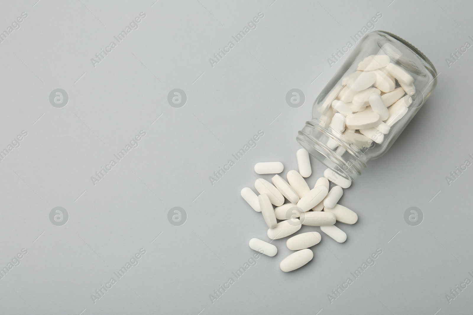 Photo of Vitamin pills and bottle on grey background, top view. Space for text