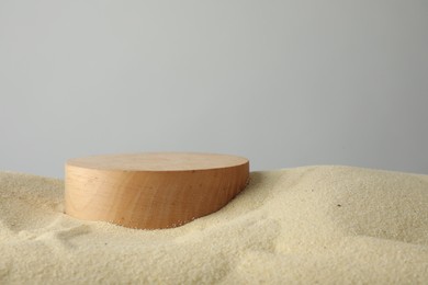 Photo of Presentation of product. Wooden podium on sand against grey background. Space for text