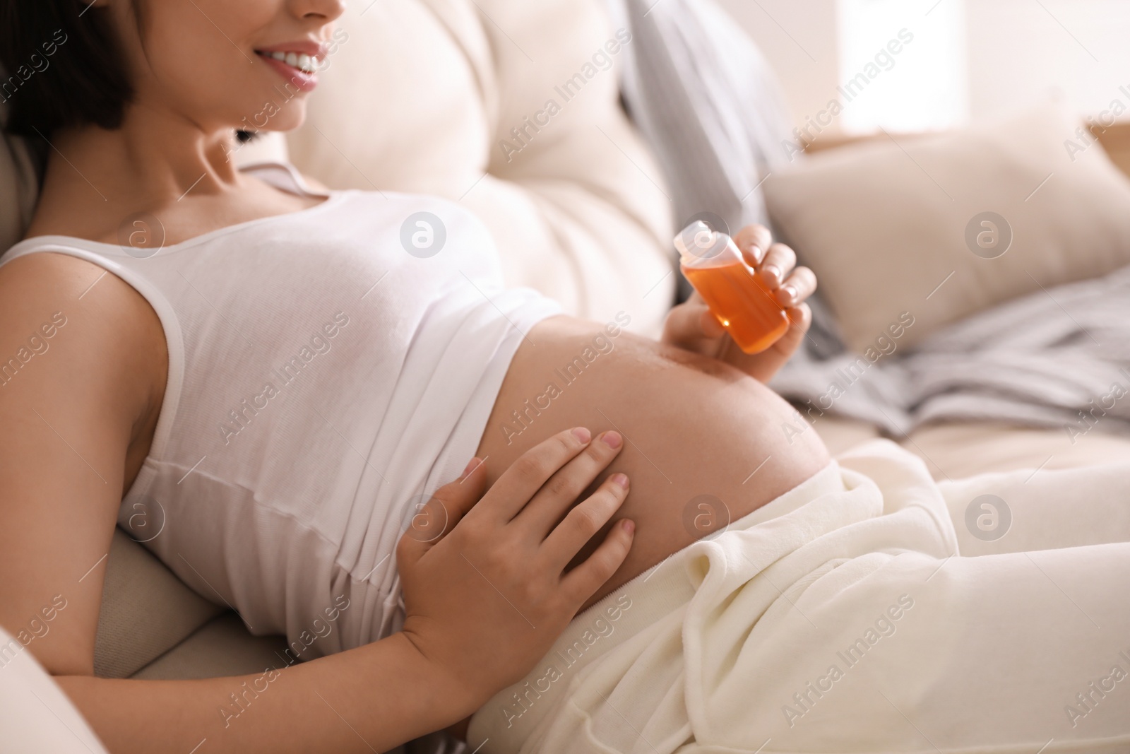 Photo of Young pregnant woman with cosmetic product on sofa indoors, closeup