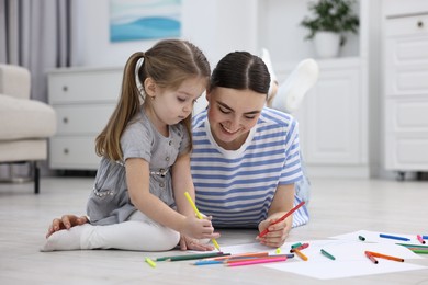 Photo of Mother and her little daughter drawing with colorful markers on floor at home