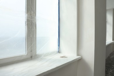 Photo of Window covered by plastic film and insulation tape indoors