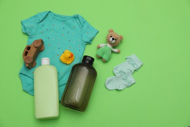 Photo of Bottles of laundry detergents, baby clothes and toys on light green background, flat lay. Space for text