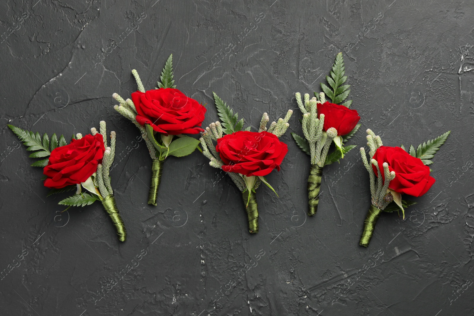 Photo of Many stylish red boutonnieres on black table, flat lay