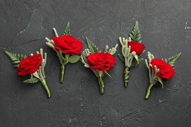 Many stylish red boutonnieres on black table, flat lay