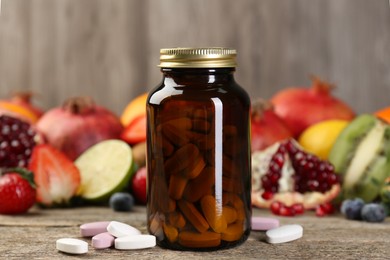 Vitamin pills, bottle and fresh fruits on wooden table