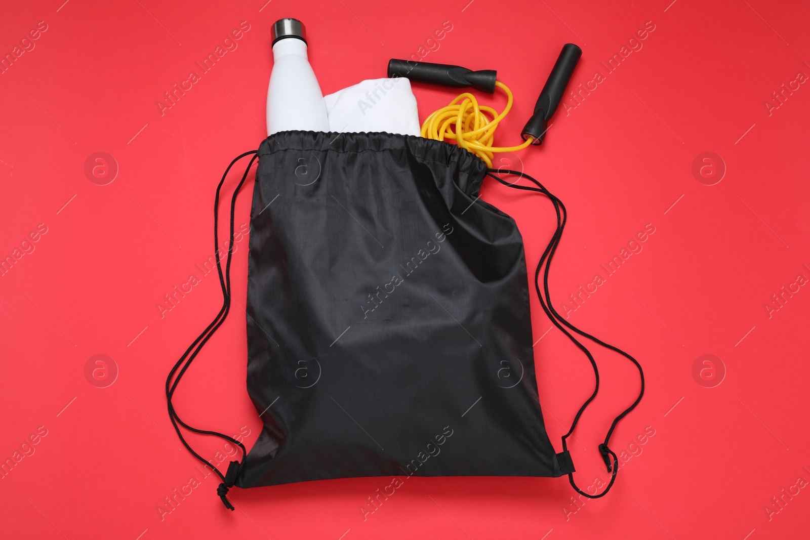 Photo of Black drawstring bag, thermo bottle and skipping rope on red background, flat lay