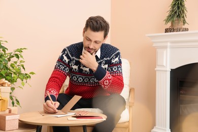Photo of Man writing wishes in Christmas greeting card in living room