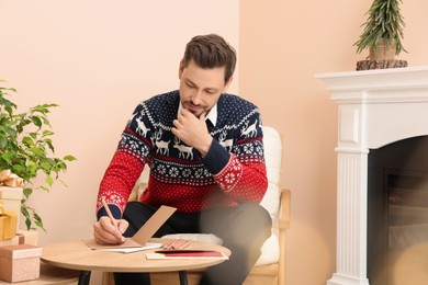 Man writing wishes in Christmas greeting card in living room