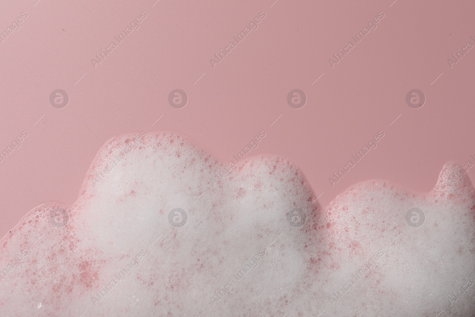 Photo of Fluffy soap foam on pink background, top view. Space for text