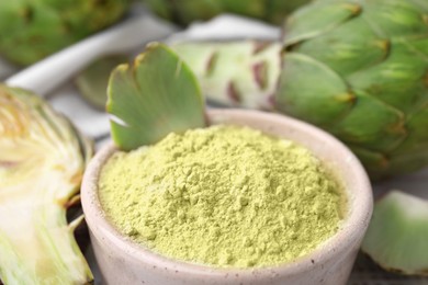 Photo of Bowl with powder and fresh artichokes on table, closeup