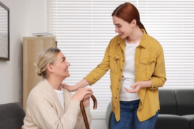 Caregiver and senior woman with walking cane sitting at home