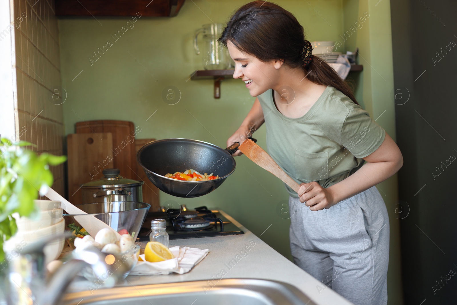 Photo of Young woman cooking vegetables in frying pan on stove indoors
