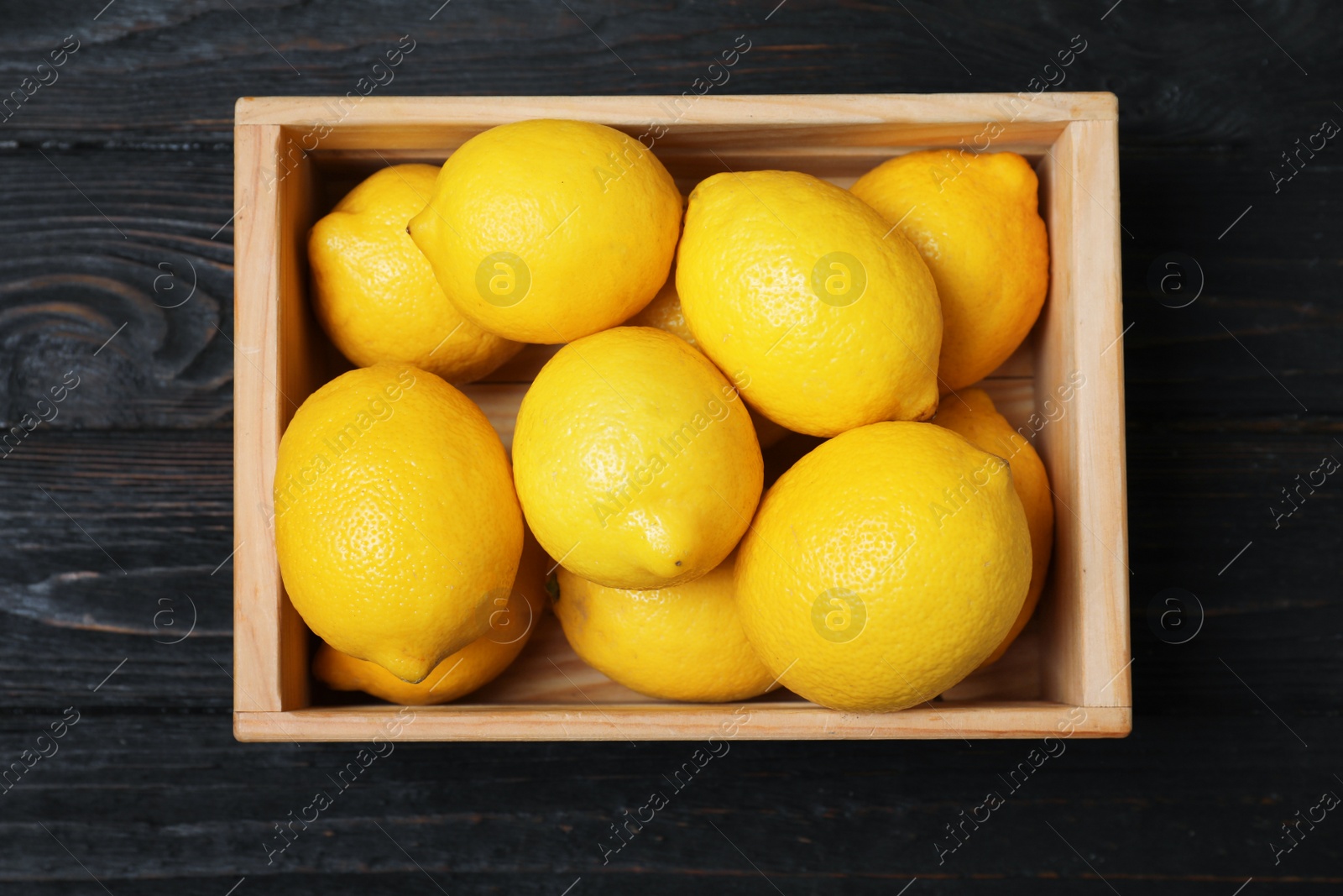 Photo of Wooden crate full of fresh lemons on dark background, top view