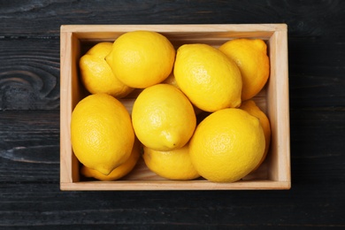 Photo of Wooden crate full of fresh lemons on dark background, top view