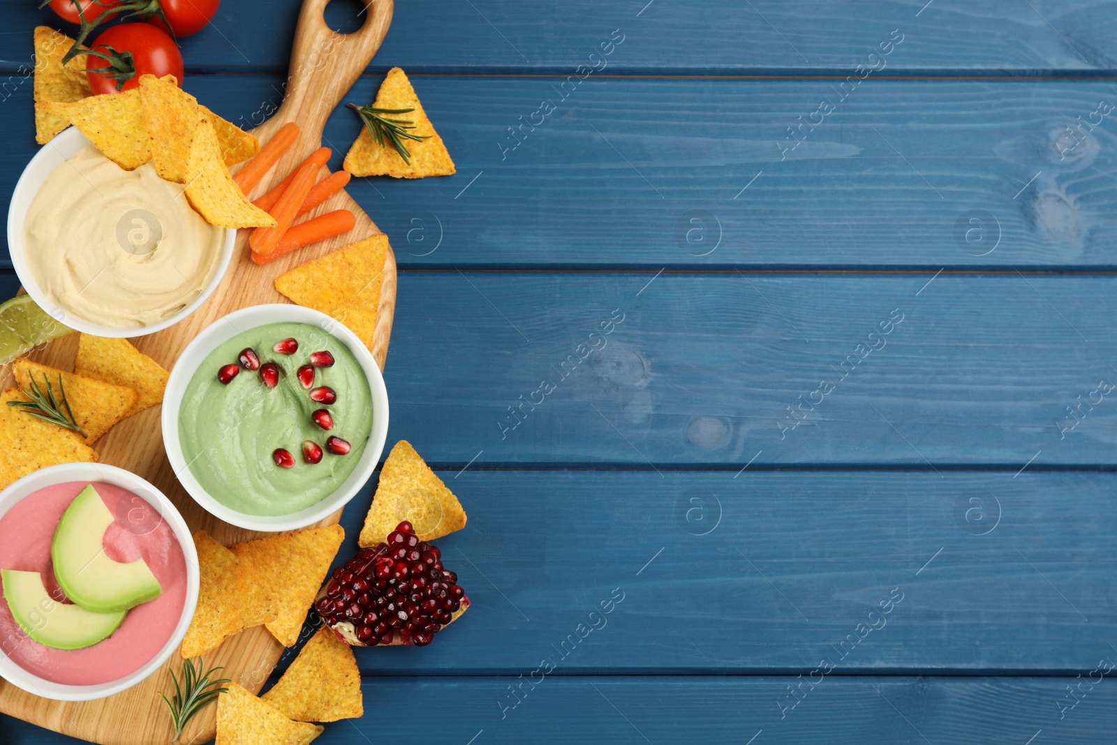 Photo of Different kinds of tasty hummus served with nachos on blue wooden table, flat lay. Space for text