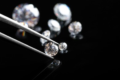 Photo of Tweezers with beautiful shiny diamond above black mirror surface, closeup