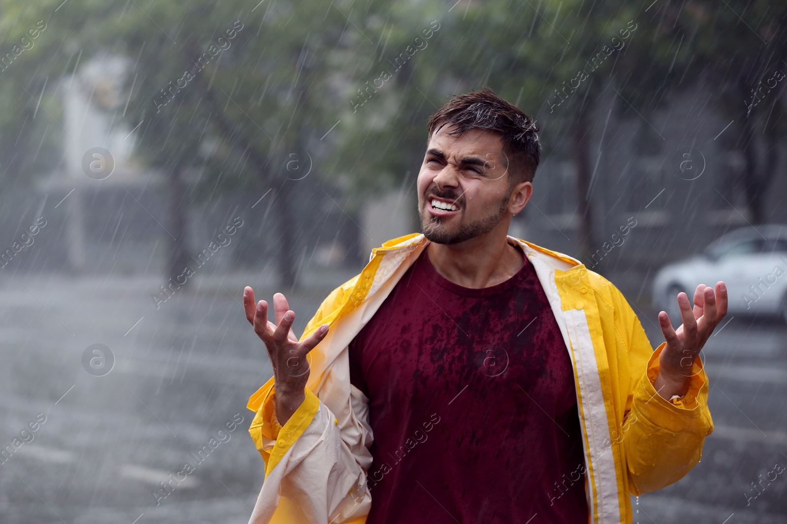 Photo of Angry young man in bright coat outdoors on rainy day