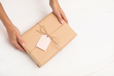 Photo of Woman holding parcel with tag and space for text on wooden background, top view