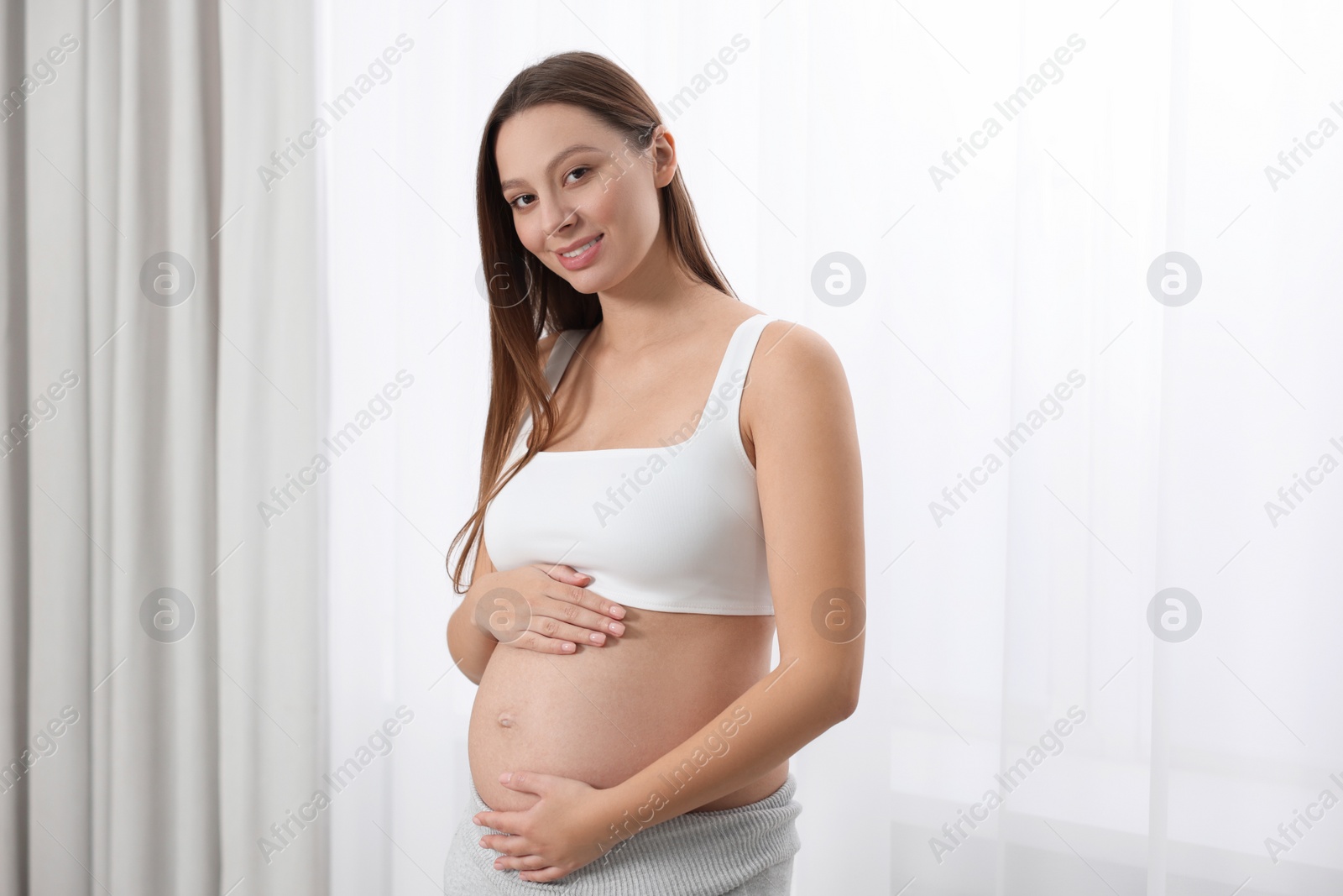 Photo of Beautiful pregnant woman with long hair near window indoors