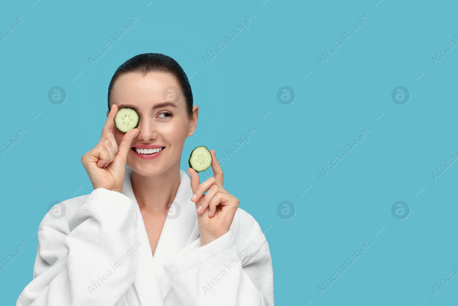 Photo of Beautiful woman covering eye with piece of cucumber on light blue background, space for text