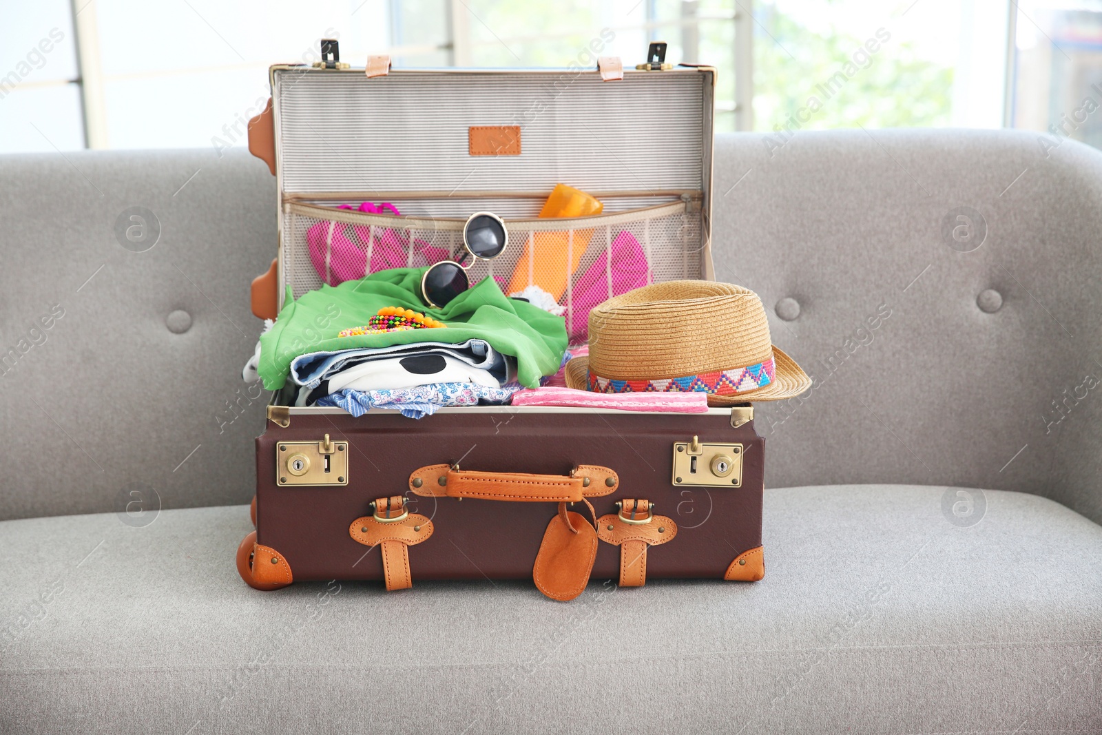 Photo of Open suitcase with different clothes and accessories for summer journey on sofa