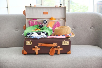 Photo of Open suitcase with different clothes and accessories for summer journey on sofa
